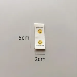 Cotton handmade folded side label with smiley face design and dimension marks for garments.