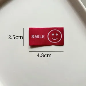 Primo piano dettagliato della toppa tessuta rossa con faccina sorridente e dimensioni.