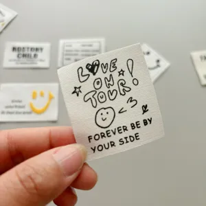 Custom clothing fabric label with trendy English letters and cute doodle designs for garments.