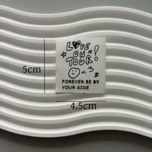 Detailed view of white fabric clothing label featuring cute letter print and smiley face design.