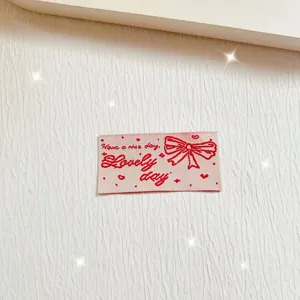 Pink woven cloth label with red bow embroidery, cute DIY sewing detail accessory.