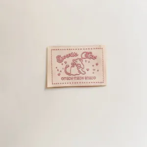 Close-up detail of a cute pink embroidered woven label with cat design for handmade crafts.