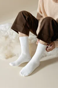 Nahaufnahme weicher weißer gerippter warmer Socken am Modell auf flauschigem Teppich.