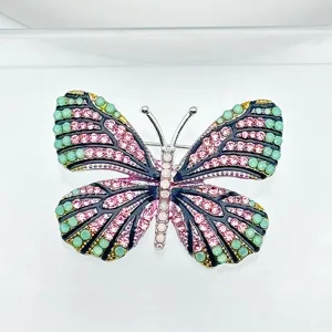 Close-up detail of a sparkling rhinestone butterfly brooch with vibrant pink and green crystals.