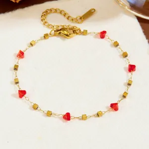 Primo piano dettagliato di un bracciale in acciaio dorato con cuori di cristallo rosso e perle.