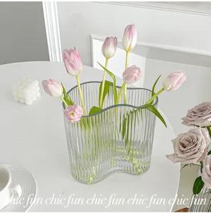 Transparent glass wavy vase detail with pink tulips, minimalist modern table decor.