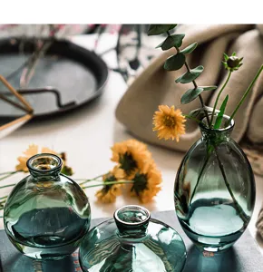 Detailed view of 3-piece green glass vase set with eucalyptus and yellow flowers on desk.