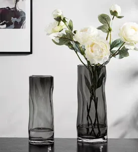 Detail shot of grey glass vases featuring wavy design with artificial white peonies floral decor.