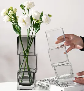 Detailaufnahme stapelbarer quadratischer Glasvasen mit frischen weißen Blumen auf modernem Tisch.