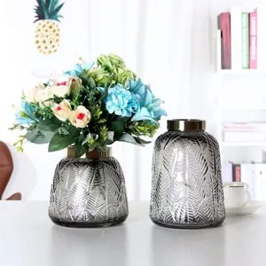 Embossed grey glass vase ornament with metal rim and flower arrangement for decor.