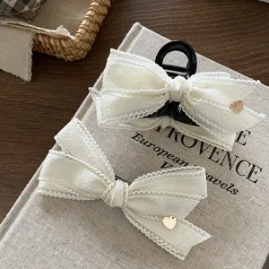 Detailed view of white fabric bow hair claw clip with charming golden heart accent, elegant styling.