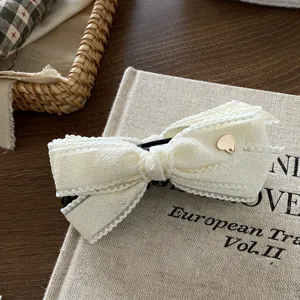 White bow hair clip detail view, elegant fabric hair claw featuring a delicate gold heart accent for women.