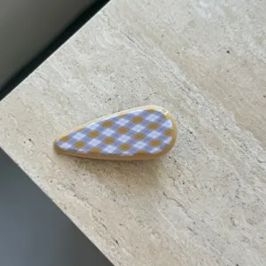 Detailansicht einer stilvollen Azetat-Haarspange in Tropfenform mit gelb-lila Rautenmuster.
