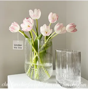 Vase en verre nordique transparent à rayures verticales et arrangement floral de tulipes fraîches.