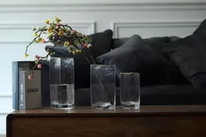 Detailed view of minimalist Nordic clear square glass vases with gold rims, styled on wood table.
