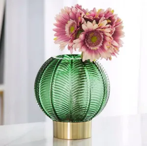 Green glass vase with gold base and pink floral arrangement for living room decor.