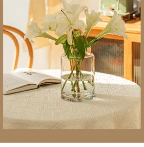 Nahaufnahme der klaren Glas-Blumenvase mit weißen Lilien auf einer strukturierten Tischdecke.
