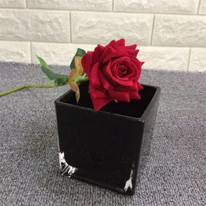 Vase en verre carré noir moderne avec rose artificielle rouge, contenant floral simple.