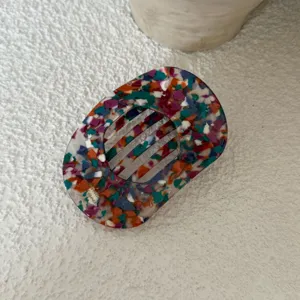 Detailopname van ovaal haarspeldje met kleurrijk terrazzo patroon, stijlvol accessoire.