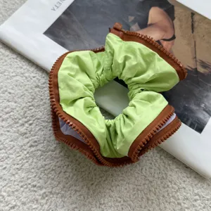 Detailed view of a stylish green hair scrunchie featuring a unique brown zipper trim.