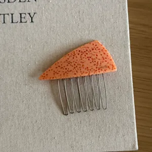 Close-up of a triangular acetate hair comb with speckled peach pattern and metal teeth.