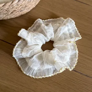 Detailed view of white sheer lace scrunchie with delicate yellow edge for elegant spring hairstyles.