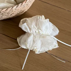 Close-up of a white sheer organza scrunchie with pearl bow detail, textured fabric.
