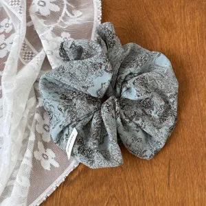 Close-up detail of a soft blue floral scrunchie with intricate pattern and handmade label.