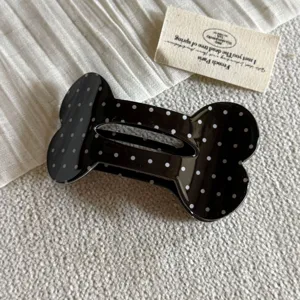 Vista dettagliata di un grazioso fermaglio per capelli nero a pois bianchi a forma di osso.