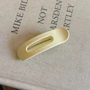 Gros plan d'une pince à cheveux bec de canard ovale jaune clair au design minimaliste.