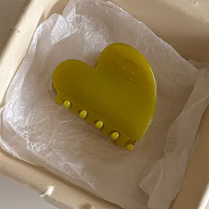 Vue détaillée de la pince à cheveux cœur en gelée vert olive posée sur du papier de soie blanc.