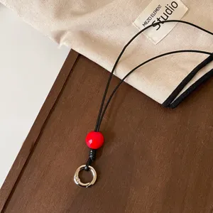 Cordón de cuero negro para gafas con cuenta roja y anillo de metal para accesorios.