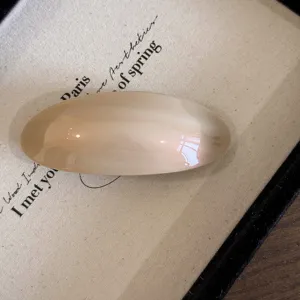 Detailopname van gladde champagne acetaat haarspeld, elegante minimalistische ovale haaraccessoire.