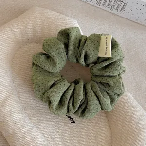 Primo piano dettagliato di un simpatico scrunchie di stoffa verde a pois con etichetta.