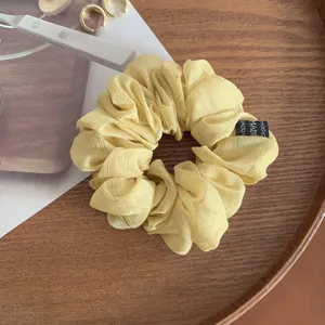 Vista dettaglio scrunchie capelli in chiffon giallo, design morbido plissettato con etichetta.