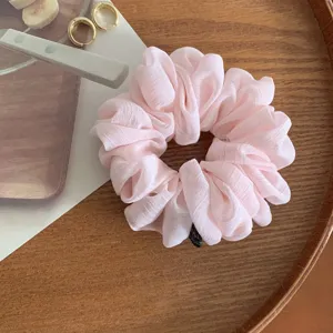Dettaglio di scrunchie per capelli in chiffon rosa, elastico morbido per styling quotidiano.