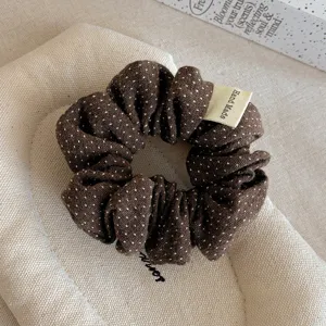 Primo piano dettagliato di un elastico per capelli in tessuto marrone a pois con etichetta.