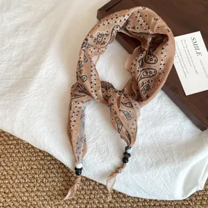 Gedetailleerde opname van een bruine sjaal met paisley-motief en kralen, stijlvol nekaccessoire.