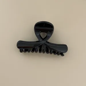 Close up of glossy black hair claw clip, featuring a stylish cross design for detailed view.