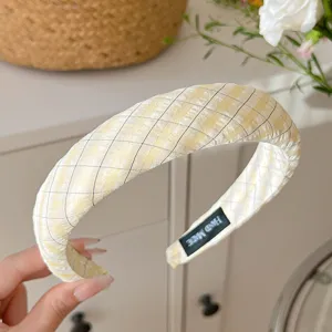 Gros plan d'un serre-tête en tissu écossais jaune, montrant une texture fine et une étiquette.