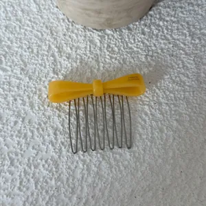 Close-up of yellow acetate bow hair comb with metallic teeth, detail shot of hair accessory.