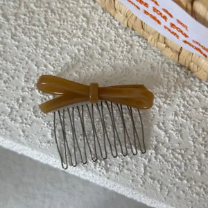 Primer plano del peine de acetato marrón con lazo y dientes metálicos, detalle.