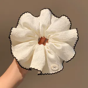 Detailed view of large white hair scrunchie featuring black lace trim and bow accent.