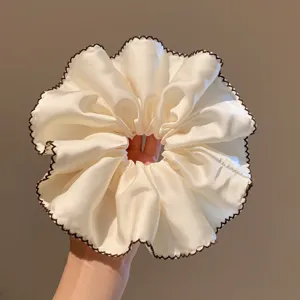 Close-up van elegante beige satijnen haarscrunchie met donkerbruine geschulpte rand.