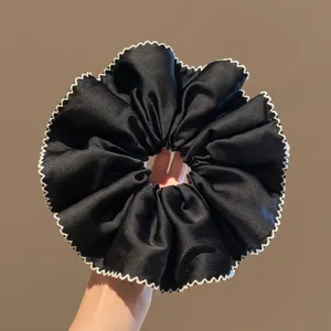 Gedetailleerde close-up van een chique zwarte satijnen haarscrunchie met witte geschulpte rand.