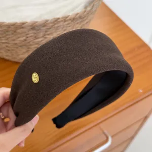 Dettaglio di un cerchietto in velluto marrone con etichetta dorata, elegante accessorio per capelli.
