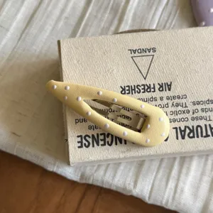 Gros plan sur la barrette à cheveux jaune à pois, surface en tissu texturé avec métal.