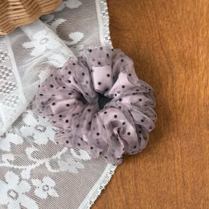 Detail shot of dusty pink polka dot mesh hair scrunchie on lace and wood background accessory