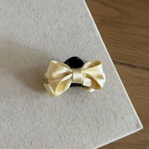 Satin bow hair claw clip detail, elegant yellow fabric bow with black plastic base for styling.