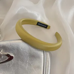 Close-up detail of the padded satin headband in light yellow, showing soft texture and handmade tag.